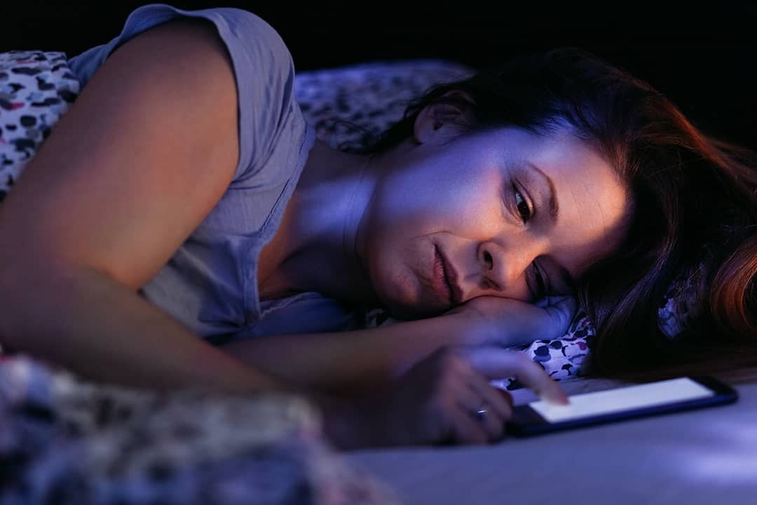 A stressed woman struggling to keep up with phone at night.